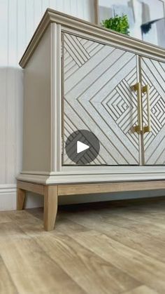 a white and gold cabinet sitting on top of a hard wood floor next to a plant