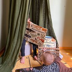 two children are sitting on the floor playing with books in front of a green curtain