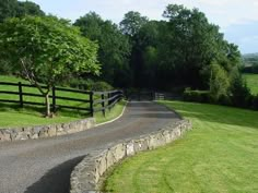 a winding road in the middle of a lush green field next to a wooden fence