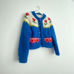 a blue cardigan sweater hanging on a white wall next to a pair of scissors