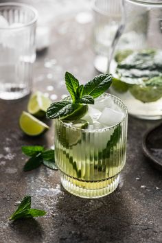 two glasses filled with ice and mint on top of a table next to limes