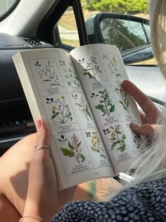 a woman sitting in a car reading a book with flowers on it's pages