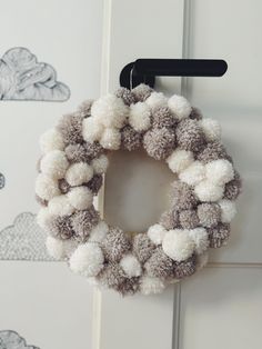 a gray and white pom - pom wreath hangs on a door handle,