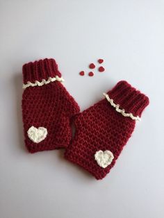 two red knitted mittens with white hearts on them next to some crochet beads