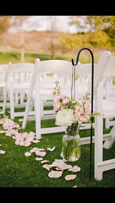 an outdoor ceremony with white chairs and flowers in vases on the aisle, along with petals scattered all over the grass