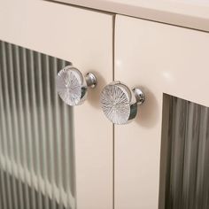 two metal knobs on the side of a white cabinet with silver foiled glass doors