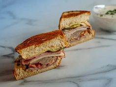 two sandwiches cut in half sitting on top of a marble counter next to a bowl