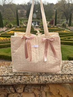 a handbag with pink bows is sitting on a stone wall in front of a garden