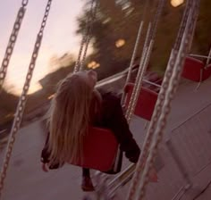 a woman is sitting on a swing in the park at sunset or dawn, with her back to the camera