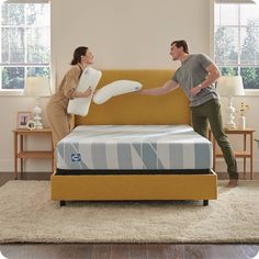 a man and woman standing next to each other in front of a bed with a mattress on it