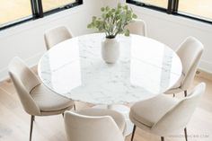 a white marble dining table with six chairs and a potted plant in the middle