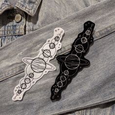 two black and white hair clips sitting on top of a jean jacket with space designs