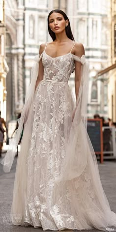 a woman is walking down the street wearing a wedding dress with an off shoulder cape