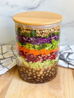 a glass jar filled with different types of salads and dressing on top of a wooden cutting board