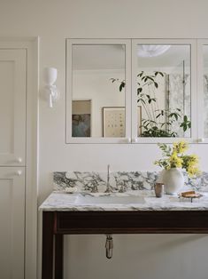 a bathroom with marble counter top and three mirrors on the wall, along with flowers