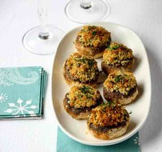 small stuffed mushrooms on a white plate next to wine glasses