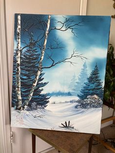 a painting is displayed on a easel in front of a door with a snowy landscape and trees