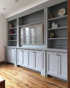 a living room with built in bookshelves and wooden flooring, along with a clock on the wall