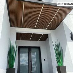 the front entrance to a modern home with potted plants on either side and an awning above it