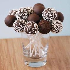 chocolate covered candies in a clear glass vase on a wooden table with white and brown sprinkles