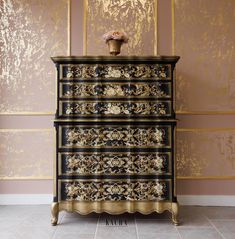 an ornate black and gold chest of drawers against a pink wall with golden trimmings