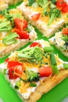 four square pieces of pizza topped with cheese and veggies on a green cutting board