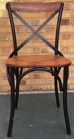 a wooden and metal chair sitting in front of a brick wall with a black frame