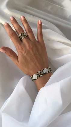 a woman's hand on top of a white sheet wearing a ring and bracelet