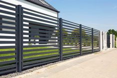 a black and white fence next to a building with grass on the side of it