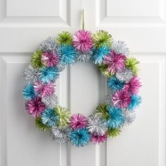 a colorful wreath is hanging on the front door with tinsel and pom - poms