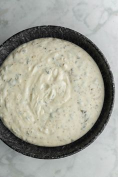 a black bowl filled with white sauce on top of a marble counter next to a spoon