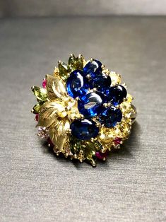 A colorful cocktail ring crafted in deep 18K yellow, gold and set with approximately 7.50cttw in oval buff top blue sapphires as well as round yellow and pink sapphires as well as green marquise shaped sapphires and .15cttw in G-I color Vs1-2 clarity round diamonds. Dimensions/Weight: Ring measures .90" in diameter and weighs 13.9g. Size 7.5 (sizable). Condition: All stones are secure and in perfectly wearable condition. R-BCCL Luxury Gold Sapphire Ring Collectible, Luxury Gold Multi-stone Sapphire Ring, Multicolor Sapphire Ring In Fine Jewelry Style, Multicolor Sapphire Multi-stone Ring, Multicolor Multi-stone Sapphire Ring, Exquisite Multi-stone Blue Sapphire Ring, Multicolor Oval Sapphire Ring For Formal Occasions, Oval Multicolor Sapphire Ring For Formal Occasions, Exquisite Blue Multi-stone Sapphire Ring