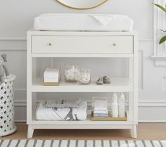 a baby changing table with white linens on it and a gold mirror above it