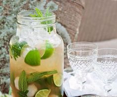 a mason jar filled with ice and limes on top of a table next to two glasses