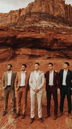 four men in suits standing next to each other on a dirt field with mountains in the background