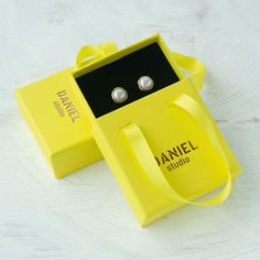 a pair of earrings in a yellow box sitting on a table next to it's packaging