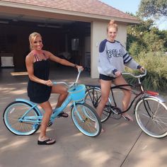 two women are riding bikes in front of a garage and one is holding the handlebars