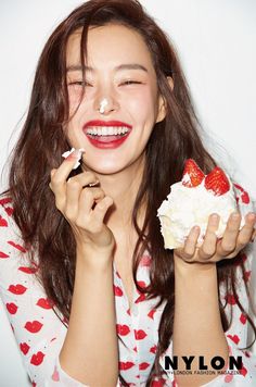 a woman holding a piece of cake with strawberries on it and whipped cream around her face