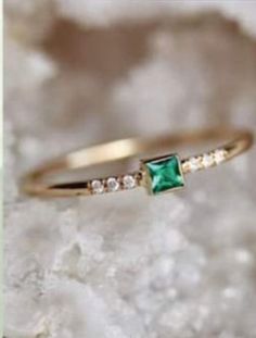 an emerald and diamond ring sitting on top of a rock