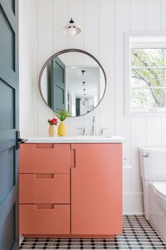 a bathroom with pink cabinets and a round mirror