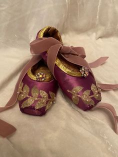 two pairs of purple shoes with gold trims and bows on white fabric covered bed