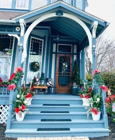 a blue house with red and white flowers on the front porch is decorated for christmas