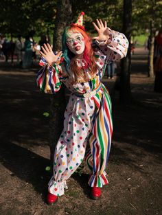 Girl in a white clown suit, half spotty, half stripey with primary colours. She has rainbow hair and a little hat and red shoes Clowncore Halloween Costumes, Clown Outfit Inspiration, Clown Outfit Reference, How To Make Clown Costume, Clowncore Outfit Drawing, Clown Halloween Costumes Cute, Cute Clown Costume Halloween, Cute Clown Outfit Aesthetic, Rainbow Clown Outfit