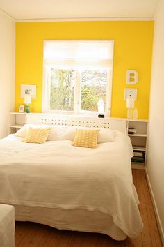 a white bed sitting in a bedroom next to a window with bright yellow paint on the walls