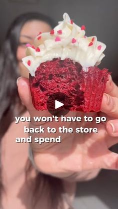 a woman holding up a red velvet cupcake with white frosting and sprinkles