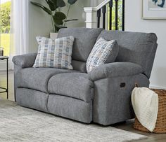 a grey couch with pillows on top of it in front of a stair case and window