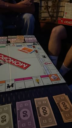 a monopoly board game sitting on top of a table next to two men playing games