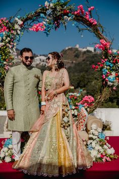 a man and woman standing next to each other in front of a floral arch with flowers