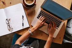 a person using a laptop computer on top of a wooden table next to a cup of coffee