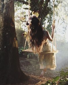 a woman swinging on a tree swing in the woods with her long hair blowing back